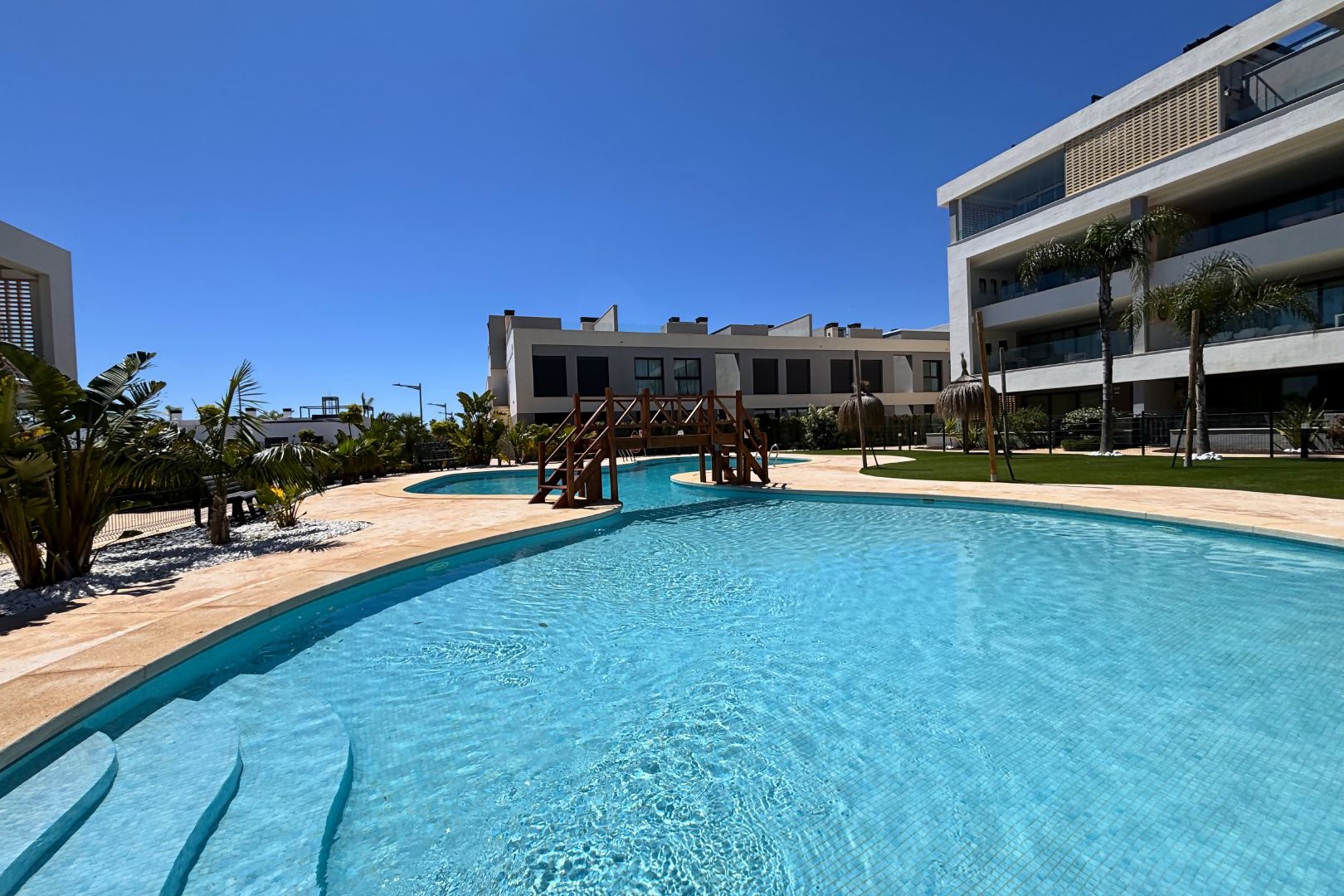 Una piscina con un pontile in legno, circondata da palme e da un edificio con balconi.