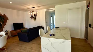 Una sala moderna con un sofá de color oscuro, un televisor de pantalla plana y un comedor con una mesa de mármol.