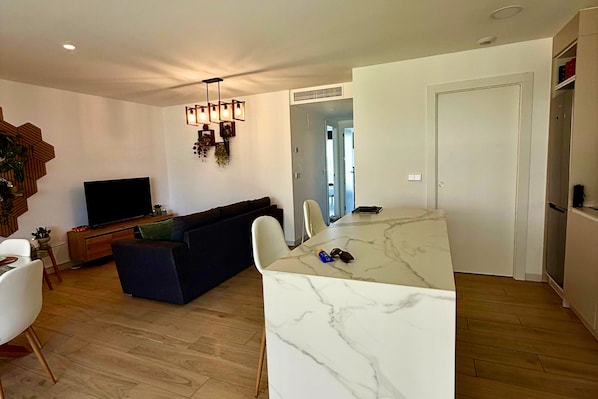 A modern living room with a dark-colored sofa, a flat-screen TV, and a dining area with a marble table. - Casa Rosalia 2 by Rental Hero (Alcazares, Los)