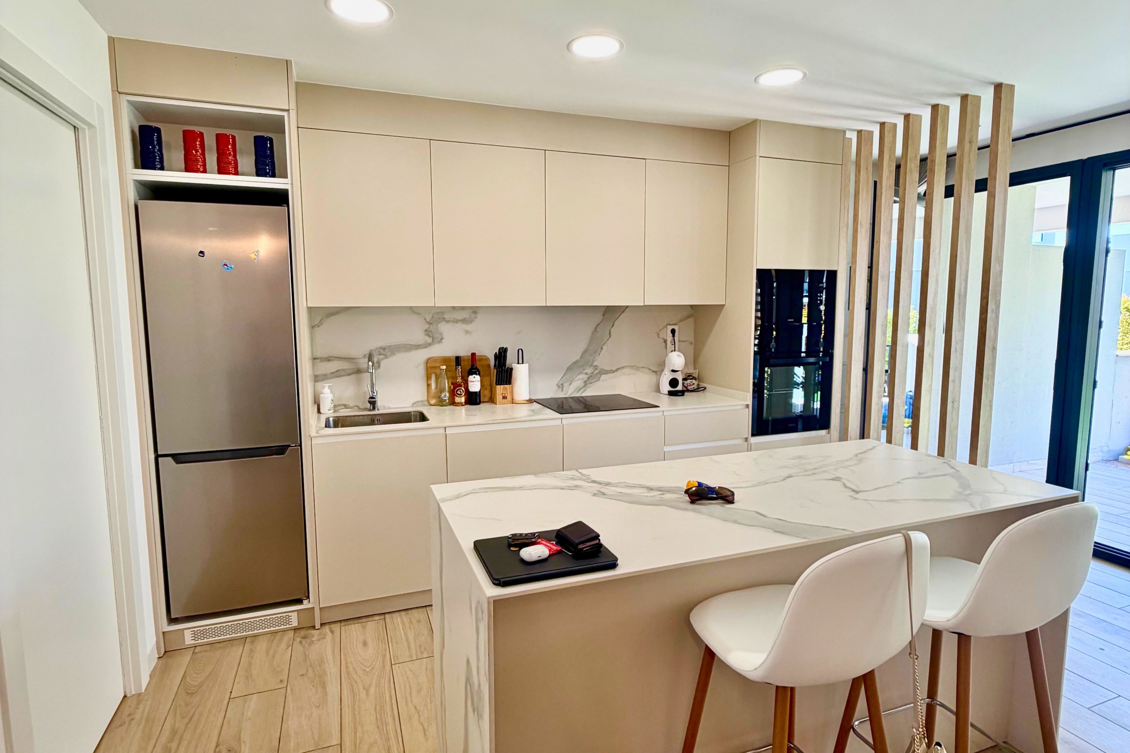 Una cocina moderna con una isla integrada, taburetes blancos y vistas al exterior.