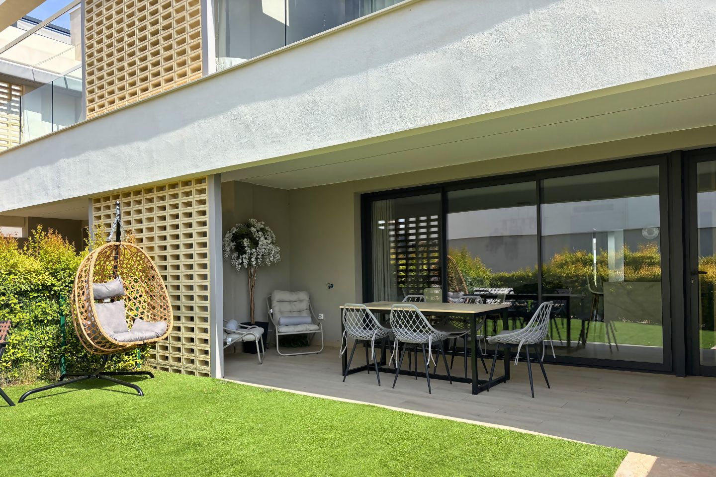 Un patio moderno al aire libre con mesa, sillas, una hamaca colgante y una planta en maceta.