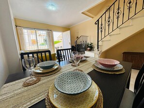 A dining area with a table set for four, a staircase, and a view of the outdoors. - Casa Brisa Mediterranea by Rental Hero (Alcazares, Los)