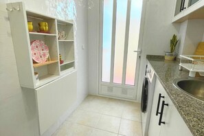 A kitchen with white cabinets, a stainless steel sink, and a window with vertical blinds. - Casa Brisa Mediterranea by Rental Hero (Alcazares, Los)