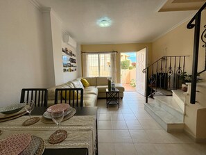 Ein Wohnzimmer mit einer Couch, einem Esstisch und Stühlen. Eine Treppe führt zu einem Außenbereich.