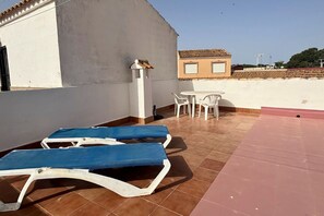 A rooftop terrace with lounge chairs, a table, and a small building in the background. - Casa Margarita by Rental Hero (Alcazares, Los)