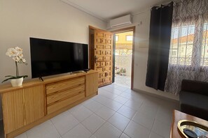 A living room with a flat-screen TV, wooden entertainment unit, potted orchid, and a view through an open door to an outdoor area. - Casa Margarita by Rental Hero (Alcazares, Los)
