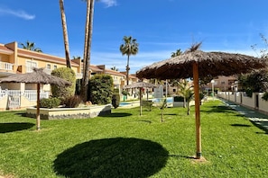 Ein Hotelinnenhof mit Palmen, einem Pool und einem strohgedeckten Gebäude.