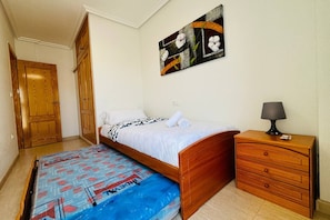 A bedroom with a wooden bed, a nightstand, a lamp, and a painting on the wall. - Casa Abuelo Fico by Rental Hero (Alcazares, Los)