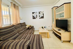 A living room with a striped sofa, a coffee table with a bottle and a plant, a flat-screen TV on a wooden stand, and two framed floral paintings on the wall. - Casa Abuelo Fico by Rental Hero (Alcazares, Los)