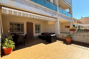 Une terrasse extérieure couverte, aménagée avec un espace repas, des sièges et des plantes en pot.