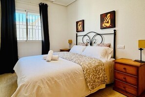 Une chambre d’hôtel comprenant un lit, une table de chevet, une commode et deux lampes fixées au mur.
