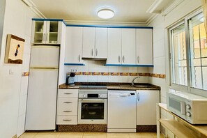 A compact kitchen with white cabinets, a built-in oven, a dishwasher, and a microwave. - Casa Abuelo Fico by Rental Hero (Alcazares, Los)