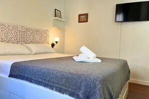 A neatly made bed with a grey blanket and white towels, a wall-mounted TV, and a decorative headboard. - Casa Paradis by Rental Hero (Alcazares, Los)