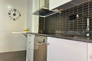 A modern kitchen with white cabinets, a black tiled backsplash, a stainless steel dishwasher, and a wall clock. - Casa Paradis by Rental Hero (Alcazares, Los)