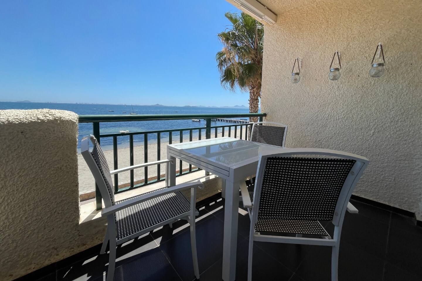 Ein Balkon mit Tisch und Stühlen, der auf ein Gewässer und eine entfernte Küste blickt.