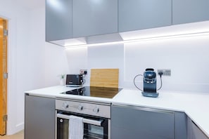 A modern kitchen with a built-in oven, a coffee machine, and a wooden backsplash. - Sleek City Stay 2 Bed Apt Free Parking and Terrace (West Yorkshire)