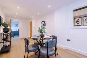 A dining area with a round table, chairs, and a vase with flowers. There is a mirror on the wall and a door leading to a kitchen. - Sleek City Stay 2 Bed Apt Free Parking and Terrace (West Yorkshire)