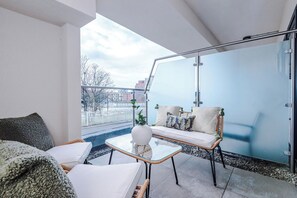 Ein moderner Balkon mit Glastrennwand, Korbmöbeln und Blick auf die Stadtlandschaft.