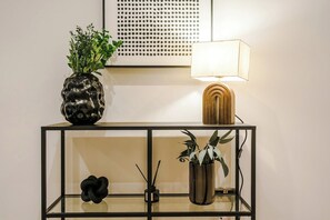 A black metal console table with a glass top, a wooden lamp, and two potted plants. - Sleek City Stay 2 Bed Apt Free Parking and Terrace (West Yorkshire)