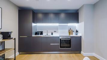 Una cocina moderna con armarios oscuros, horno empotrado y cafetera.