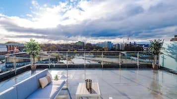 Una terraza en la azotea con vistas al horizonte urbano, una zona de estar con mesa y una barandilla.