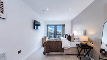 Un dormitorio moderno con una cama, mesita de noche, lámpara y televisor montado en la pared.