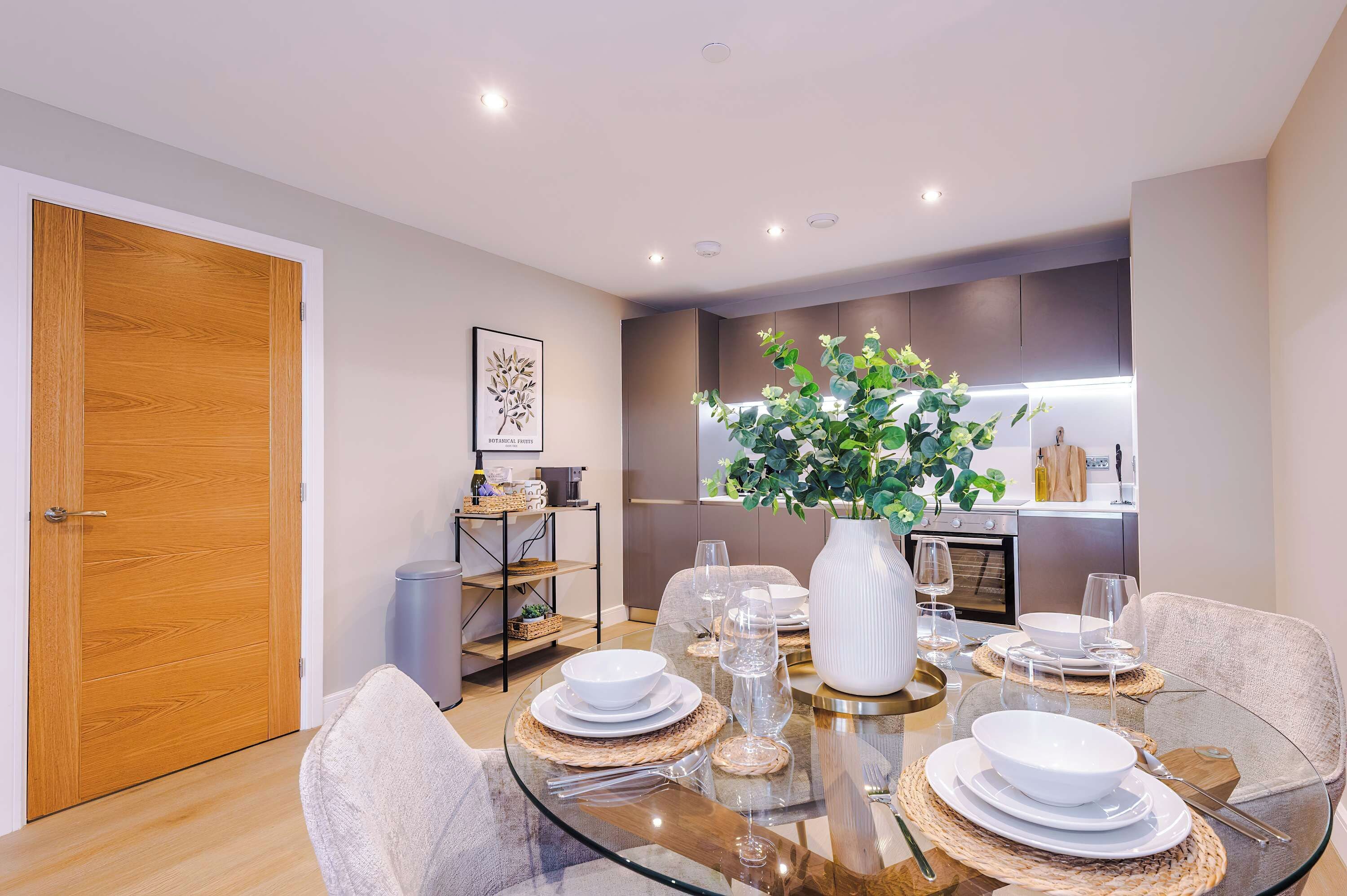 Un comedor moderno con una mesa de vidrio, platos blancos y un jarrón con plantas verdes.