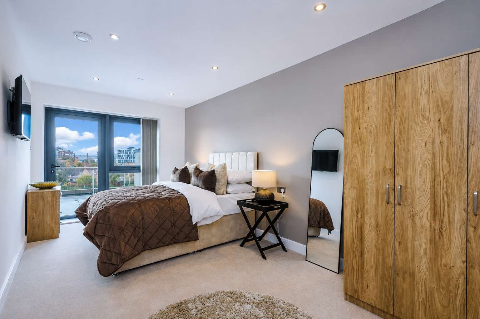 A bedroom with a large bed, a bedside table with a lamp, a mirror, and a wardrobe.