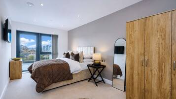 A bedroom with a large bed, a bedside table with a lamp, a mirror, and a wardrobe.