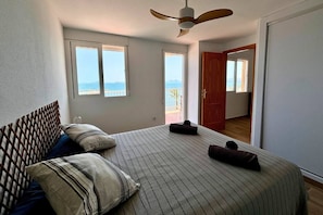 Een slaapkamer met een bed, een plafondventilator en uitzicht op zee door het raam.