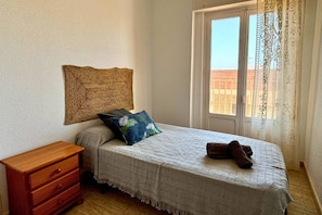 A bedroom with a bed, a wooden nightstand, a woven wall hanging, and a window with curtains. - Casa Playa de la Concha by Rental Hero (Alcazares, Los)