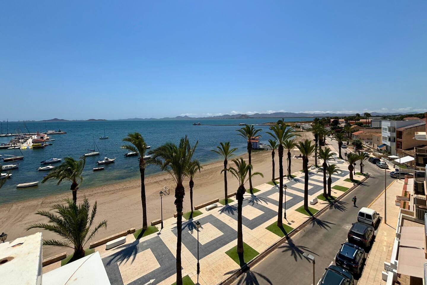 A coastal view with a beach, palm trees, and boats.