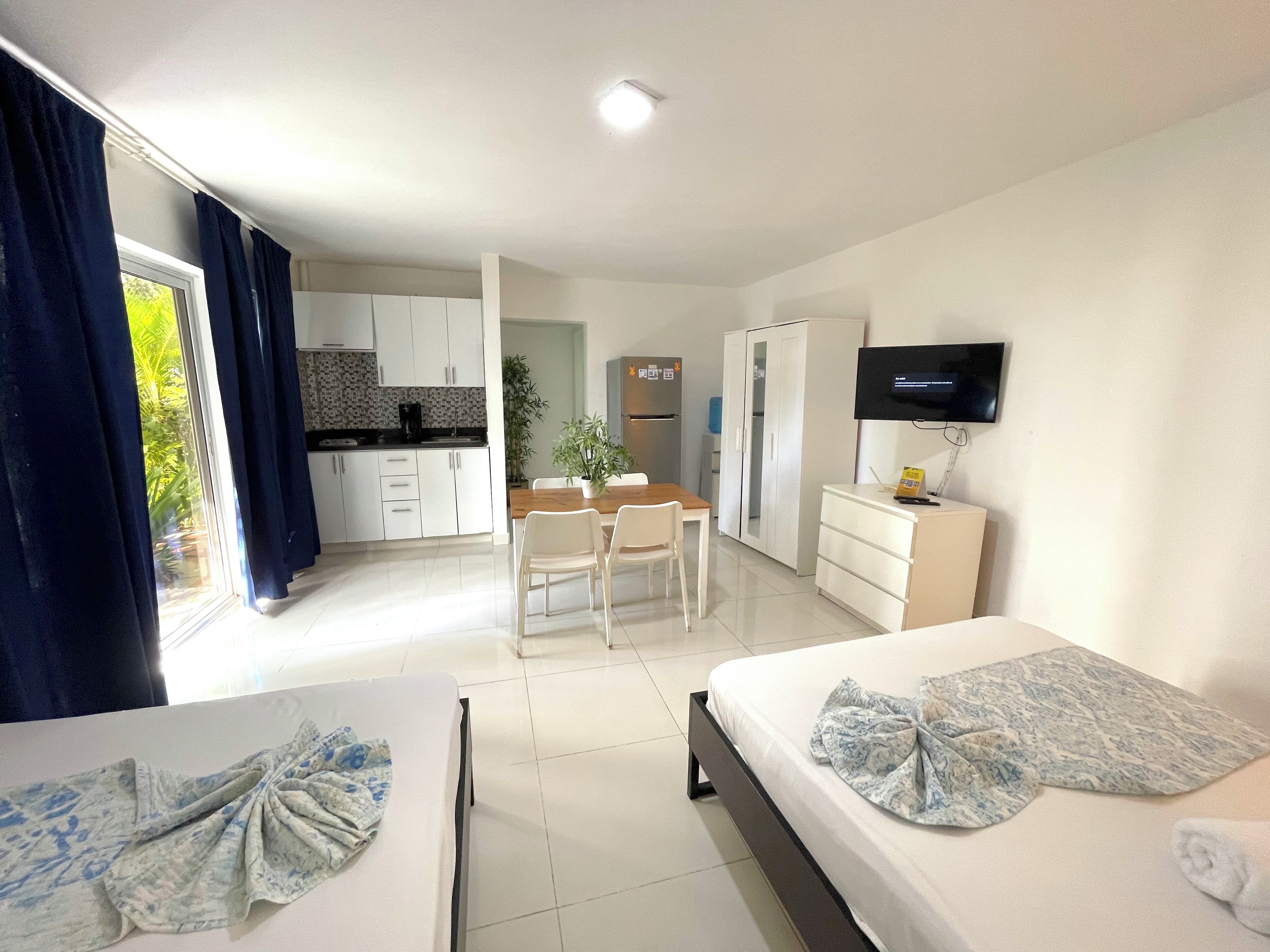 A hotel room with two beds, a TV, a desk, and a kitchenette.