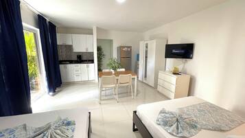 A hotel room with two beds, a TV, a desk, and a kitchenette.