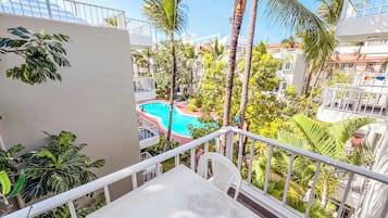 Een balkon met uitzicht op een zwembad, omringd door palmbomen en ander groen.