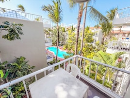 A balcony with a view of a swimming pool surrounded by palm trees and other greenery.