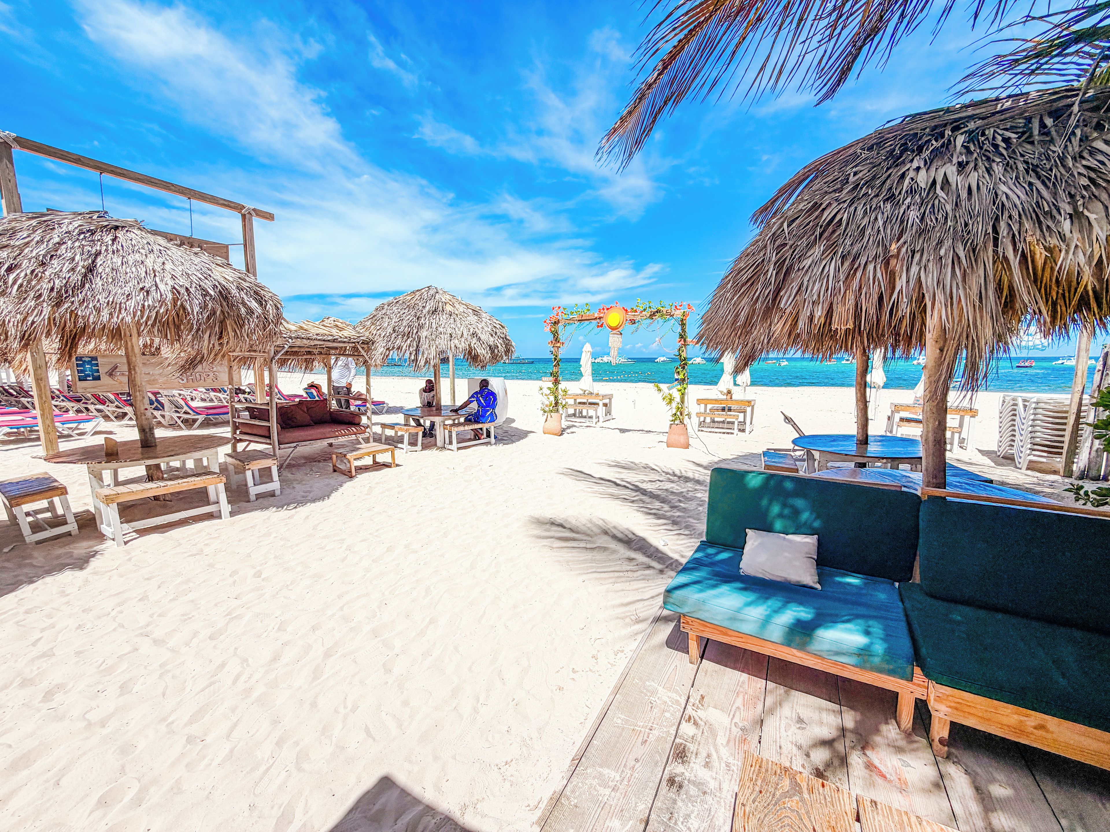 Een terras aan het strand met rieten parasols, zitplaatsen en uitzicht op de oceaan.