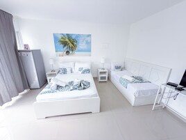 A hotel room with two beds, a refrigerator, a TV, and a painting of a beach scene.
