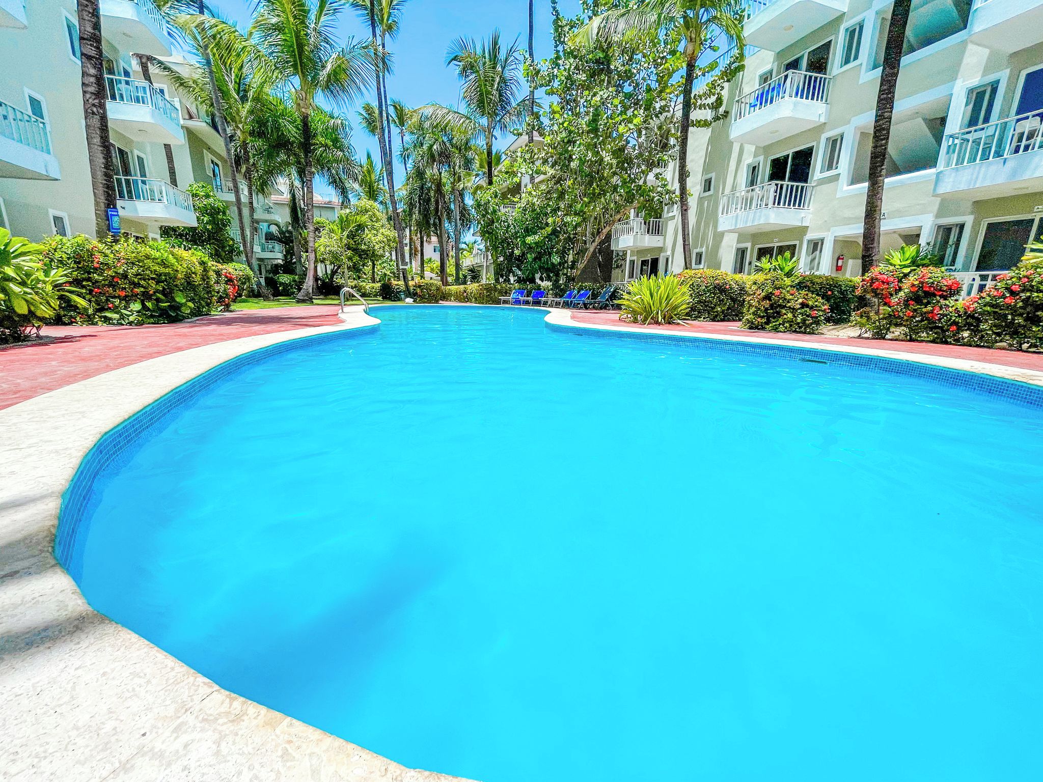 A swimming pool surrounded by palm trees and a building with balconies.