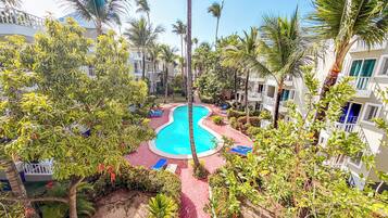 A pool area surrounded by lush greenery and palm trees, with a clear blue sky above.
