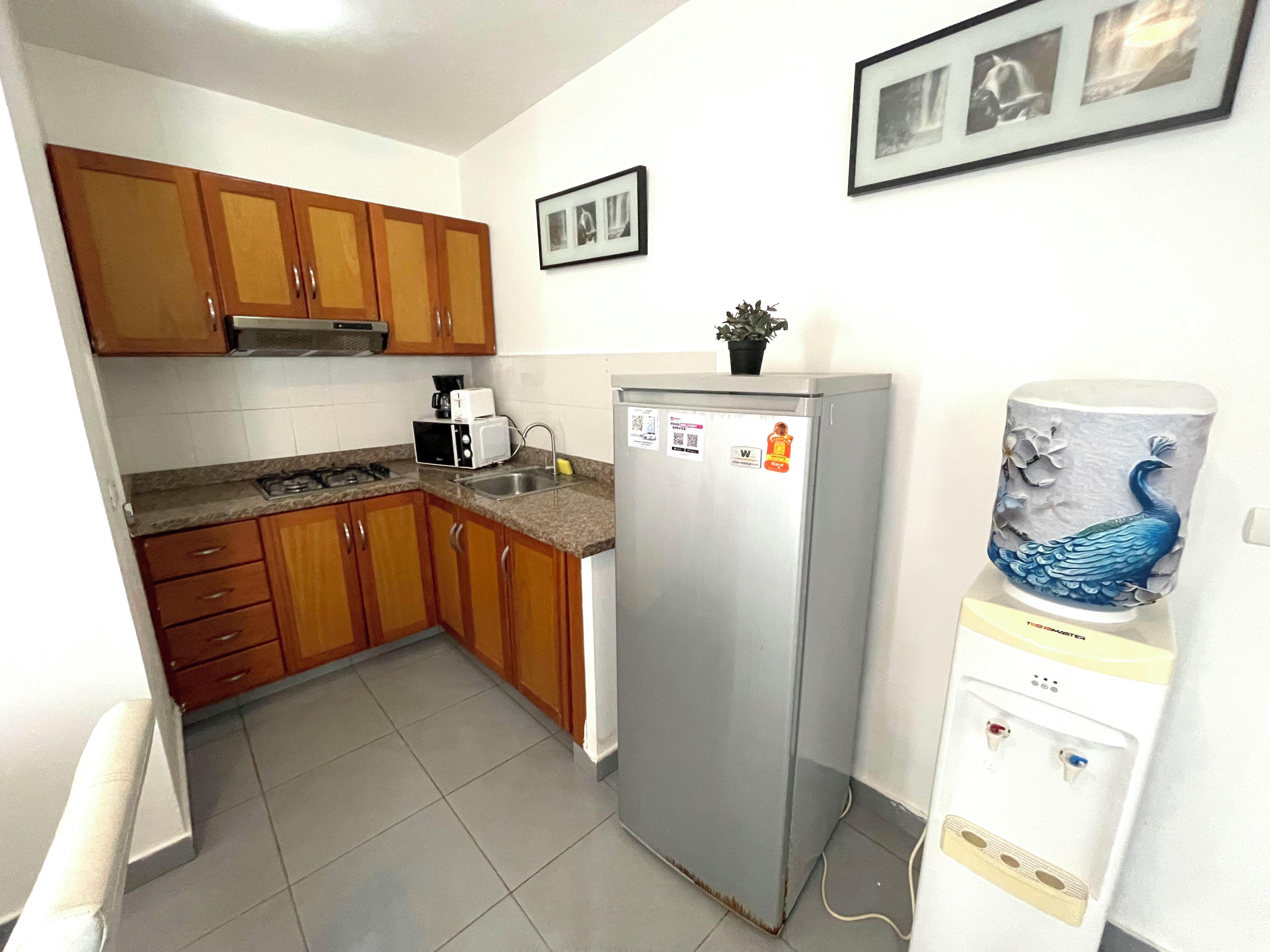 Een kleine keuken met houten kastjes, een roestvrijstalen koelkast, een waterdispenser en een magnetron.