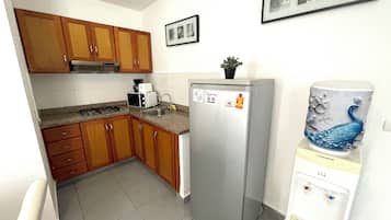 Een kleine keuken met houten kastjes, een roestvrijstalen koelkast, een waterdispenser en een magnetron.