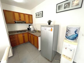 A compact kitchen with wooden cabinets, a stainless steel refrigerator, a water dispenser, and a microwave. - VACATION STUDIOS and SUITES playa BAVARO (Punta Cana)