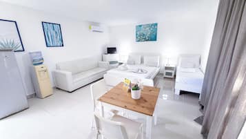 Una habitación de hotel moderna con cama, mesitas de noche, sofá, mesa de comedor con sillas, dispensador de agua y obras de arte en las paredes.