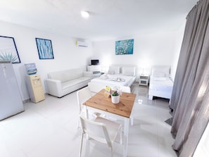 A modern hotel room with a bed, bedside tables, a sofa, a dining table with chairs, a water dispenser, and artwork on the walls. - VACATION STUDIOS and SUITES playa BAVARO (Punta Cana)