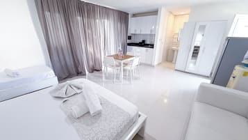 Una habitación de hotel moderna con una cama, una mesita y una kitchenette al fondo.