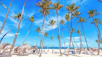 Una playa con altas palmeras y sombrillas de paja.