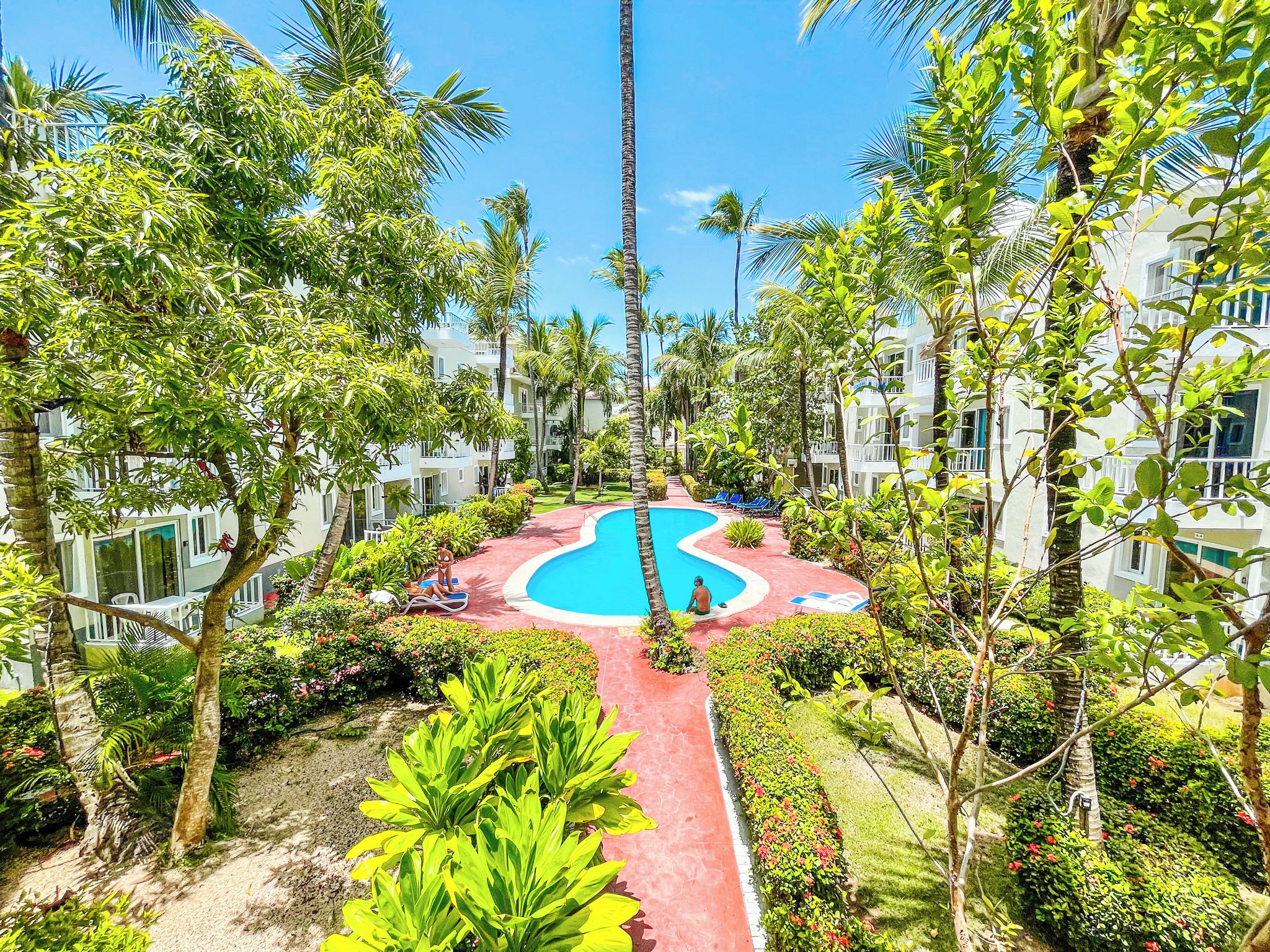 Een resort met een centraal gelegen zwembad, omringd door weelderige begroeiing en palmbomen.