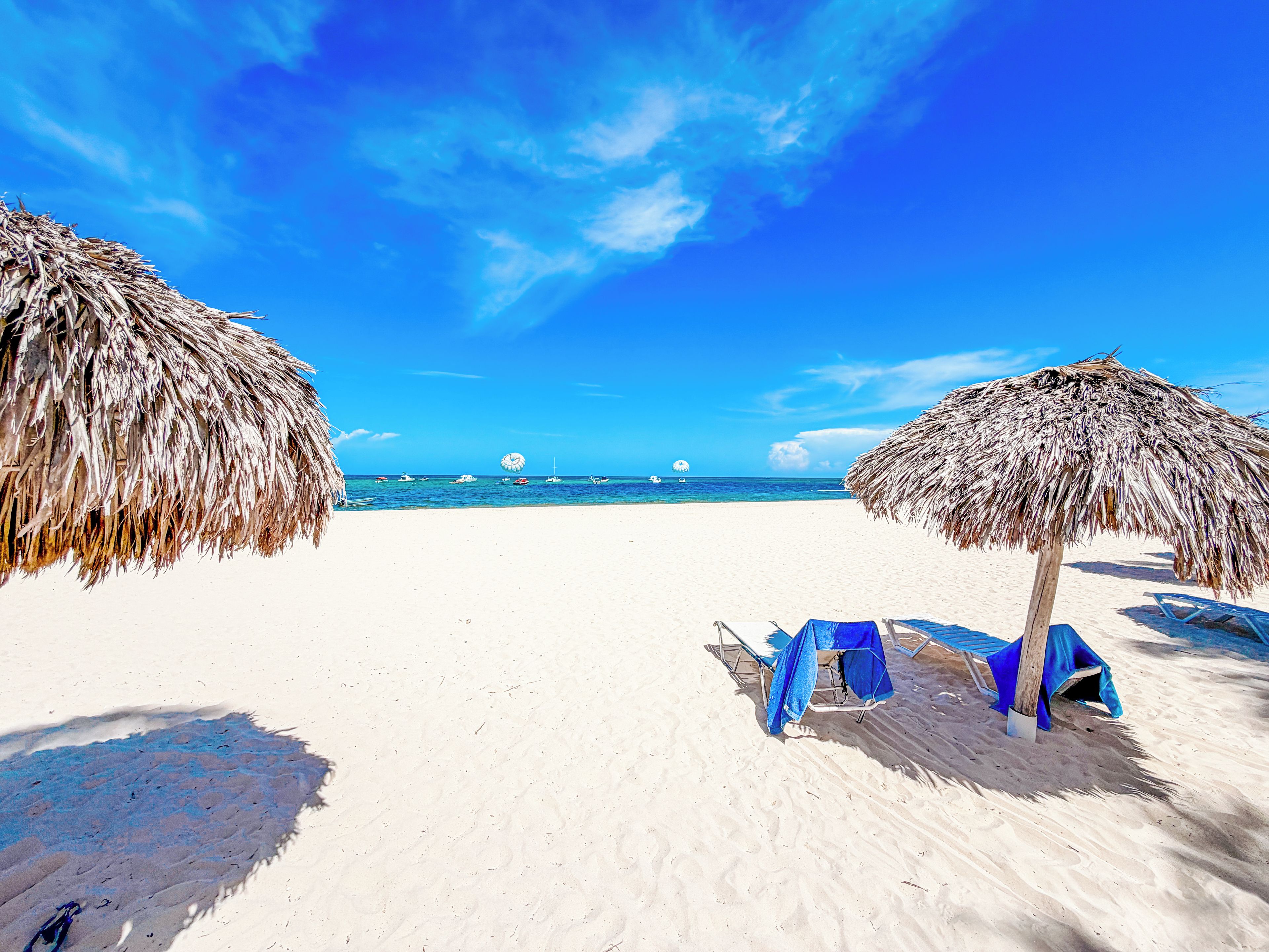 Een strand met rieten parasols, een zandstrand en een helderblauwe lucht.