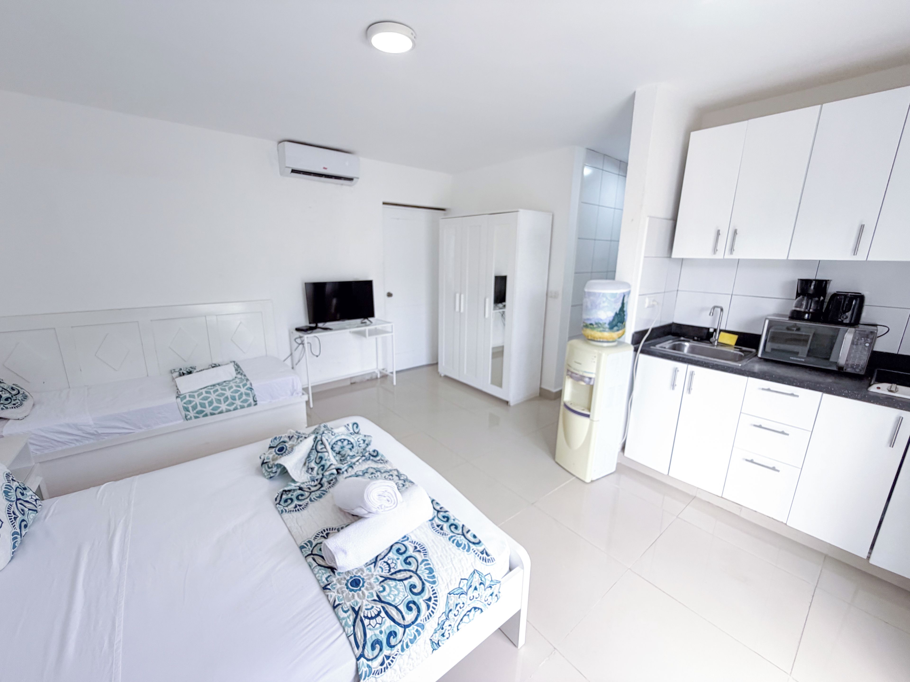 Une chambre d’hôtel équipée d’un lit, d’une télévision, d’un distributeur d’eau et d’une kitchenette.